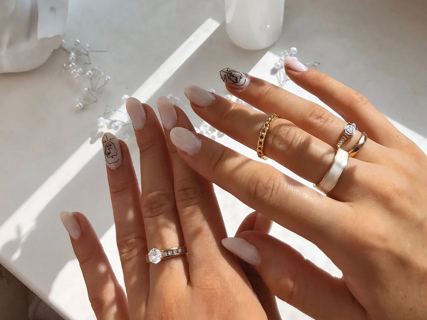 Hands with milky nails, line-art nail design and gold rings